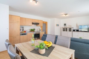 A modern kitchen with wooden cabinets, a dining table with chairs, and a television in the background. - Holiday apartment with 1 bedroom (Ahlbeck (Seebad))