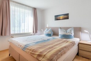 A bedroom with a bed, a bedside table, a nightstand, a window with curtains, and a wall-mounted picture. - Holiday apartment with 1 bedroom (Ahlbeck (Seebad))