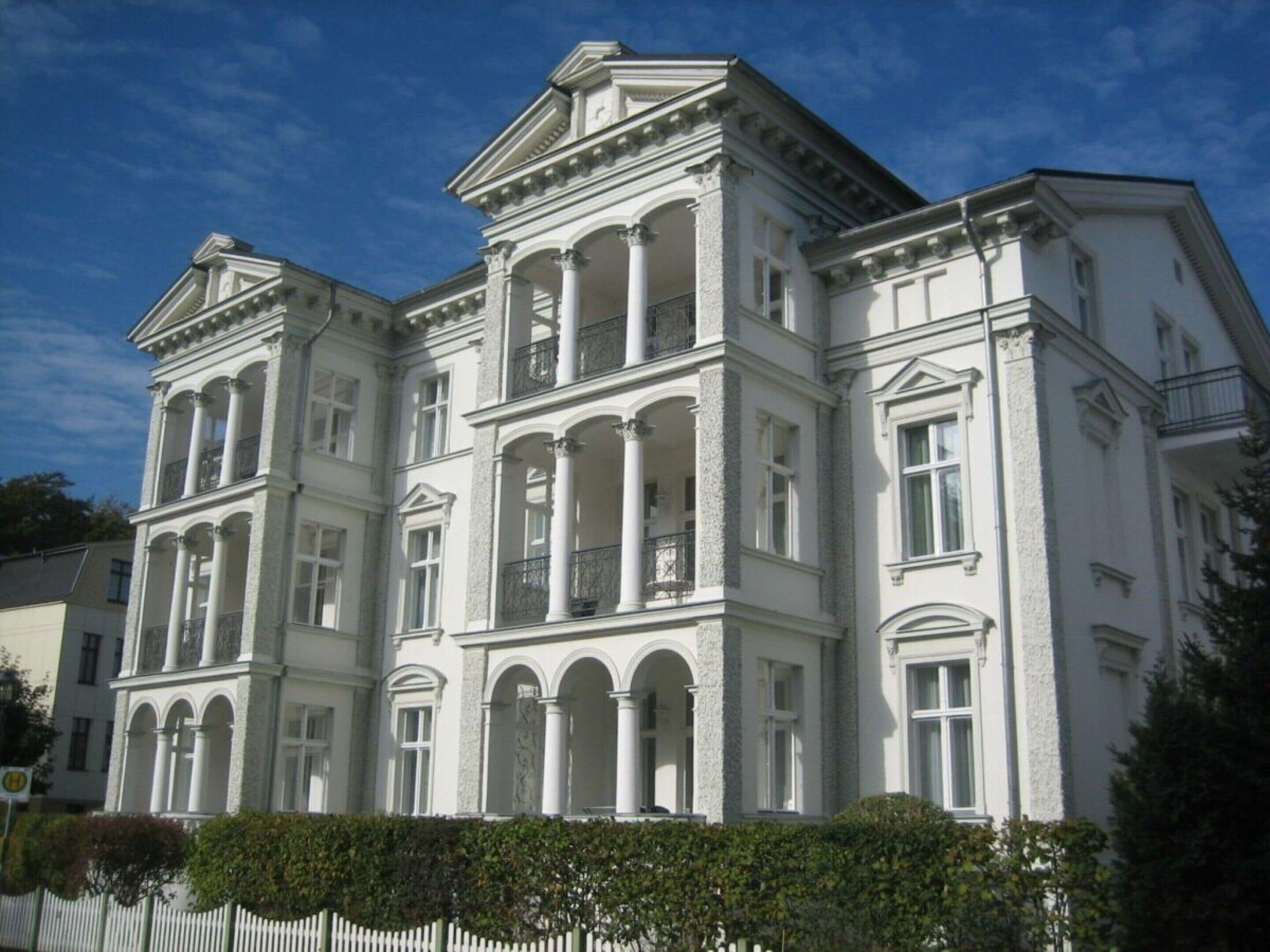 A large, white, classical-style building with multiple balconies and arched windows.