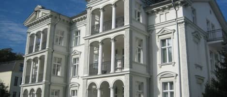 A large, white, classical-style building with multiple balconies and arched windows.