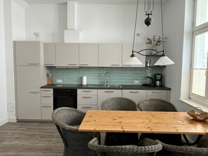 Eine moderne Küche mit weißen Schränken, einem Holztisch, Korbstühlen und Pendelleuchten.