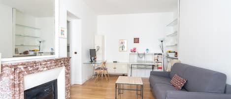 Una sala de estar con chimenea, un sofá gris, una mesita y una estantería.