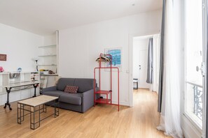 Una sala de estar moderna con un sofá gris, una mesita, un estante de metal rojo y una pared blanca con un cuadro enmarcado.
