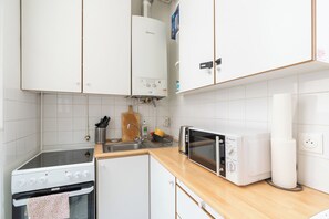 A kitchen with white cabinets, a stove, a microwave, and a sink. - Cozy 1BDR Apartment for 4 Near Champs-Elysees (Paris)