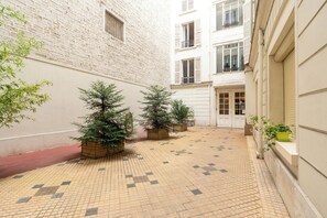 A narrow alley with tiled flooring, potted plants, and a building with a brick facade and multiple windows. - Cozy 1BDR Apartment for 4 Near Champs-Elysees (Paris)
