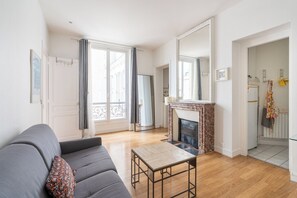 A living room with a sofa, a fireplace, and a view of the outside. - Cozy 1BDR Apartment for 4 Near Champs-Elysees (Paris)