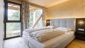 Un dormitorio con una cama grande, paredes de madera, un ventanal con cortinas y vistas a árboles.