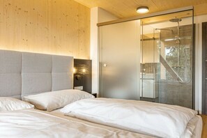 A modern bedroom with a large bed, a glass shower enclosure, and a wooden ceiling. - Superior Chalet #16 with Sauna & Hot Tub (Turrach)