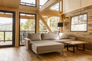 Ein modernes Blockhaus-Interieur mit einer Eckcouch, einem kleinen Tisch und großen Fenstern mit Blick ins Freie.