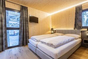A room with a bed, a TV mounted on the wall, and a window with curtains. - Superior Chalet # 9 with Sauna & Hot Tub (Turrach)