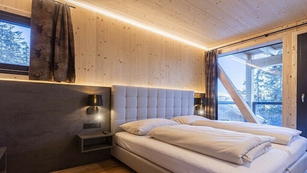 Quarto com cama grande, paredes de madeira, mesa de cabeceira e janela com cortinas.