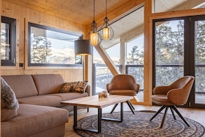 Un interior acogedor con techo de madera, ventanas amplias, un sofá, dos sillones y una mesa.