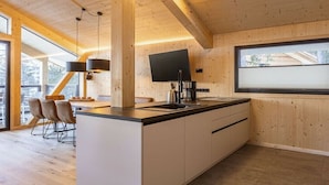 Uma cozinha moderna com interior em madeira, uma janela grande e uma área de refeições com cadeiras.