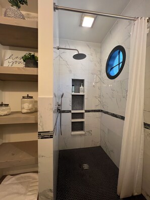Een douche met een rond raam, een handdoekhouder en een plank met toiletartikelen.