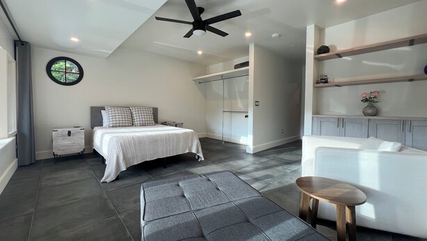 Quarto moderno com cama, mesa de cabeceira e ventilador de teto.