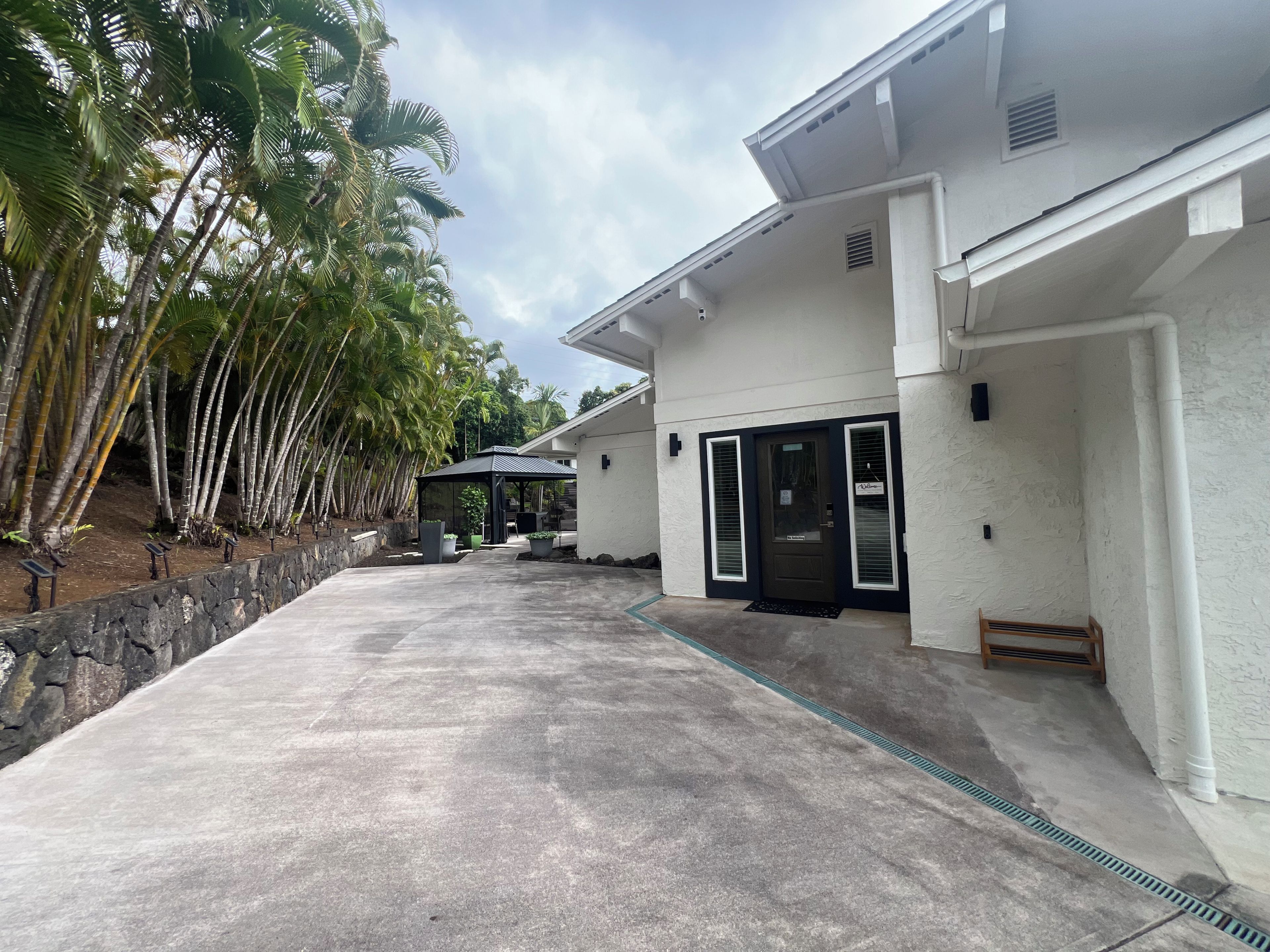 A modern building with a concrete driveway, a covered outdoor seating area, and a stone retaining wall.