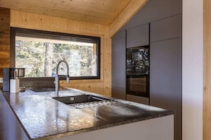 A modern kitchen with a granite countertop, stainless steel sink, and a built-in oven. - Superior Chalet #1 with Sauna & Hot Tub (Turrach)