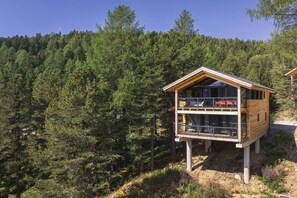Eine zweigeschossige Holzhütte mit Balkon, umgeben von dichtem Wald.