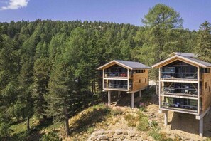 Two wooden cabins with balconies, situated on a rocky outcrop surrounded by dense forest. - Superior Chalet #1 with Sauna & Hot Tub (Turrach)