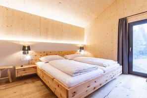 A wooden room with a bed, bedside tables, and a window. - Superior Chalet #1 with Sauna & Hot Tub (Turrach)
