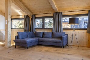 Ein Zimmer mit einer Eckcouch, einer Stehlampe und großen Fenstern mit Vorhängen.