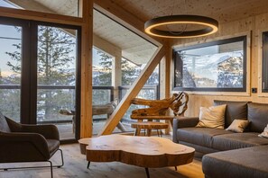 A modern interior with a wooden ceiling, large windows, a wooden coffee table, and a sofa. - Superior Chalet # 8 with Sauna & Hot Tub (Turrach)
