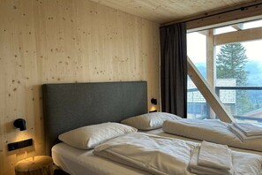 A room with a bed, a headboard, a wall-mounted light, and a window with curtains. - Superior Chalet # 8 with Sauna & Hot Tub (Turrach)