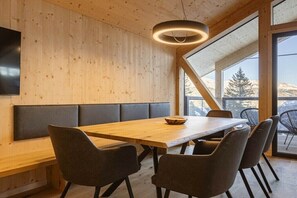 A modern dining area with a wooden table, black cushioned bench seating, and a large window offering a view of the outdoors. - Superior Chalet # 8 with Sauna & Hot Tub (Turrach)