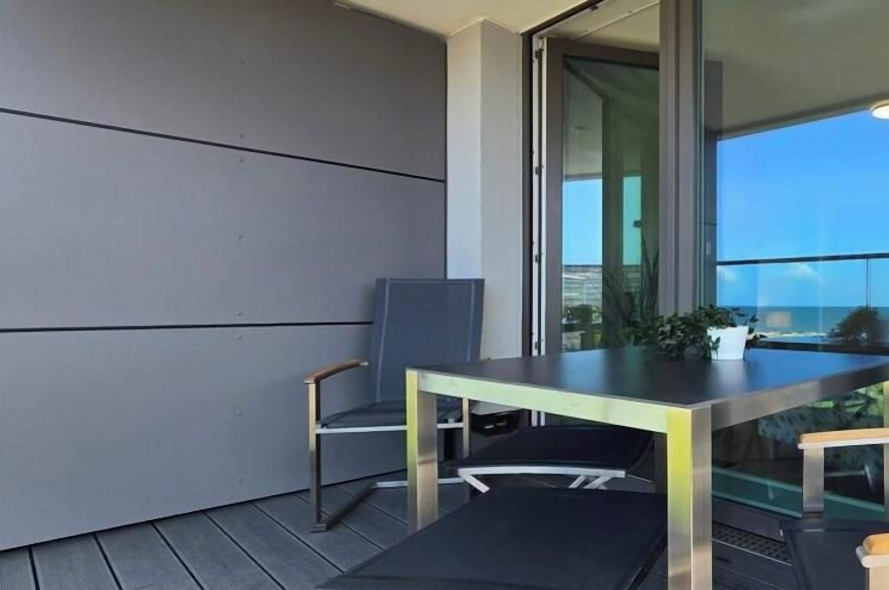 Ein Balkon mit Tisch und Stühlen, eine Schiebetür und Blick zum Himmel.