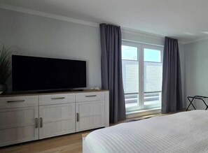 A bedroom with a bed, a television on a cabinet, and a window with curtains. - Holiday apartment i15 - "Sea Rush" (Graal-Müritz)