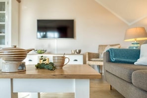Ein modernes Wohnzimmer mit einem wandmontierten Flachbildfernseher, einem Holztisch mit Dekoration, einer blauen Couch und einer Lampe.