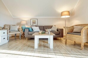 A cozy living room with a sofa, two wicker chairs, a coffee table, and a floor lamp. - Holiday apartment with 1 bedroom (Zingst)