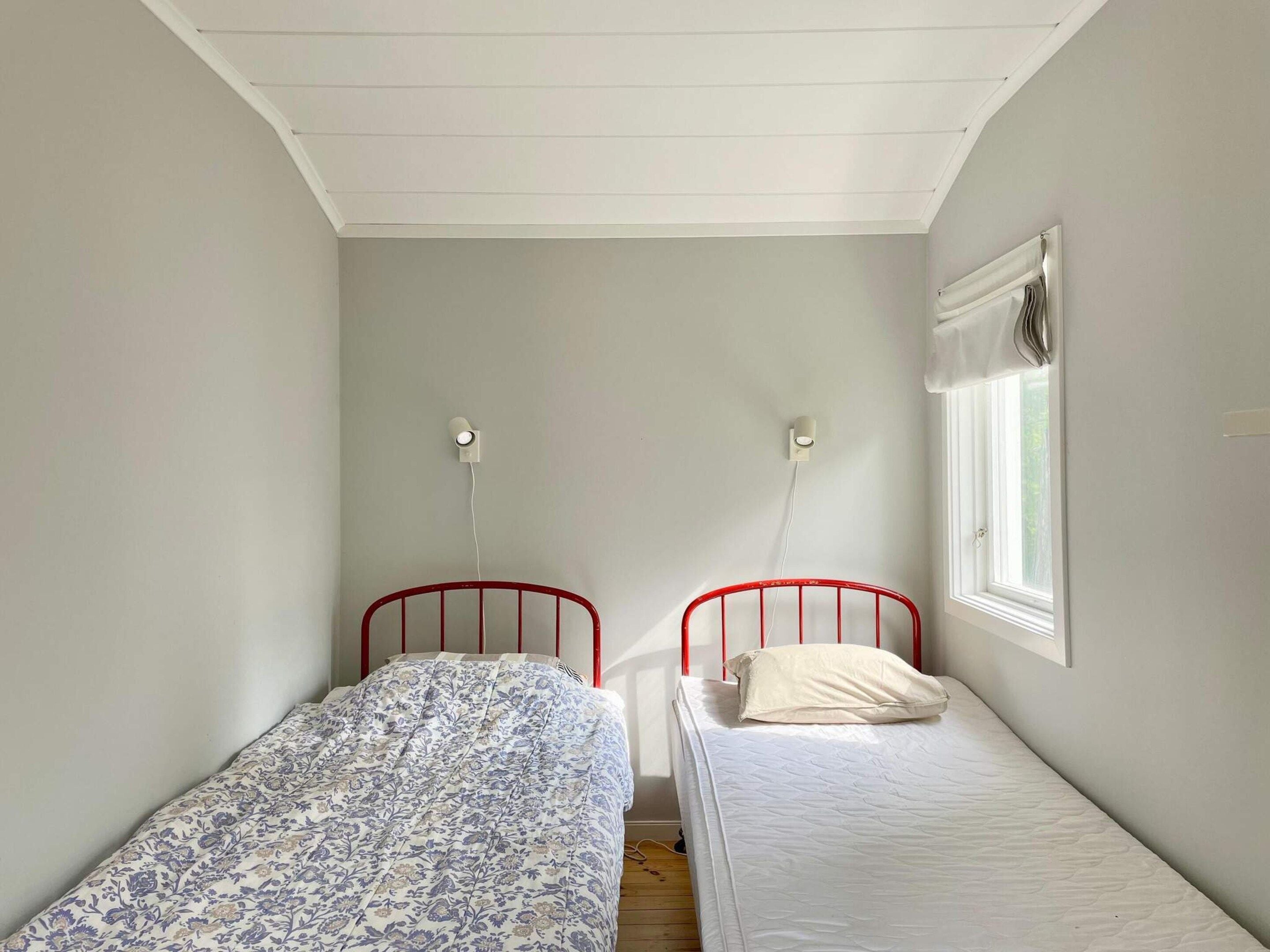 Un petit logement composé d’une seule pièce, comprenant deux lits simples, une fenêtre avec un store et un plafond à pente.