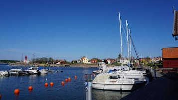 Un puerto deportivo con barcos amarrados, un faro al fondo y casas a lo largo de la costa.