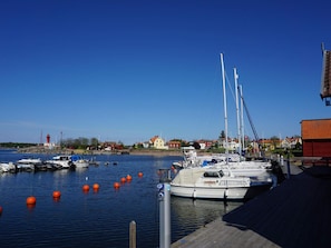 A marina with boats docked, a lighthouse in the background, and houses along the shore.