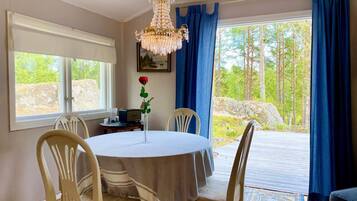Un coin repas avec une table ronde, des chaises, un lustre, un vase de roses et une vue sur l’extérieur.