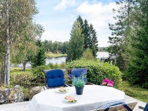 Ein Essbereich im Freien mit einem Tisch für zwei Personen, umgeben von Grünpflanzen und Blick auf einen See.