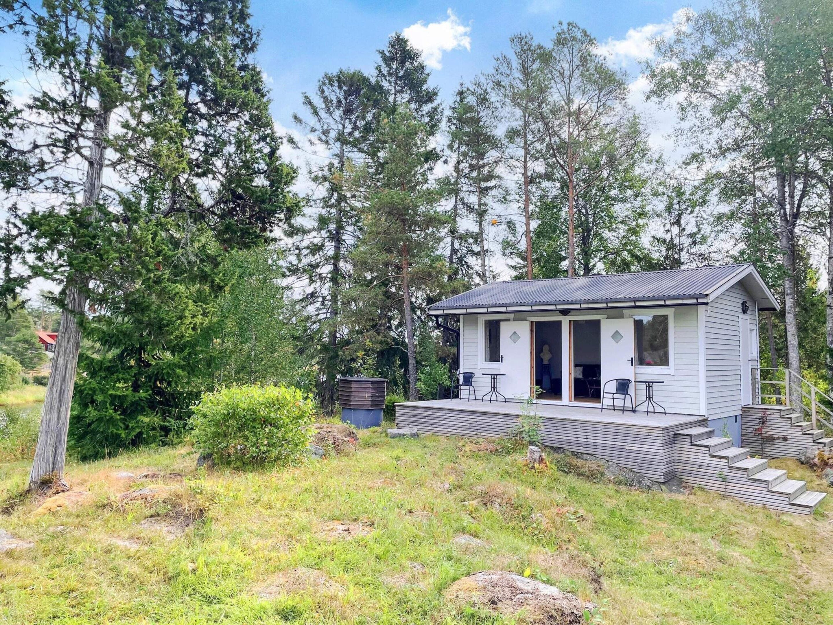 A small cabin with a porch, surrounded by trees and a grassy area.