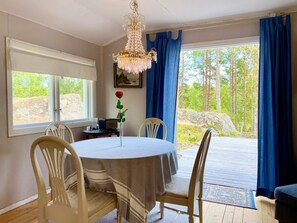 Un coin repas comprenant une table ronde, des chaises, un lustre, une fenêtre avec des rideaux et une vue sur les arbres.