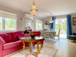 A room with a red sofa, a glass-top table, and a chandelier. There is a dining table with chairs and a window with curtains.