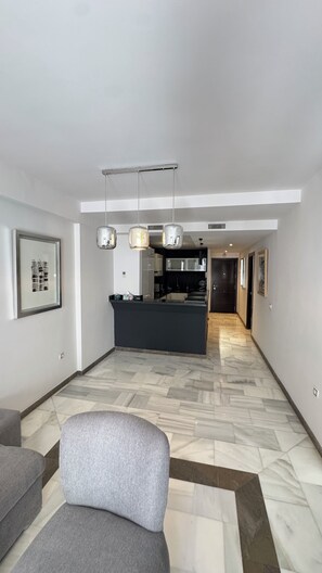 A modern living room with a grey sofa, a kitchen area in the background, and a patterned floor. - Luxury pool and great location (Tanger)