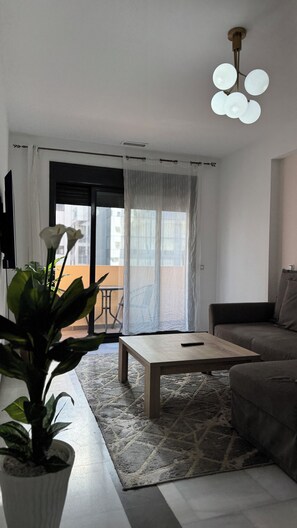 Ein modernes Wohnzimmer mit einer Couch, einem Couchtisch, einer Topfpflanze und einem Balkon mit Blick.