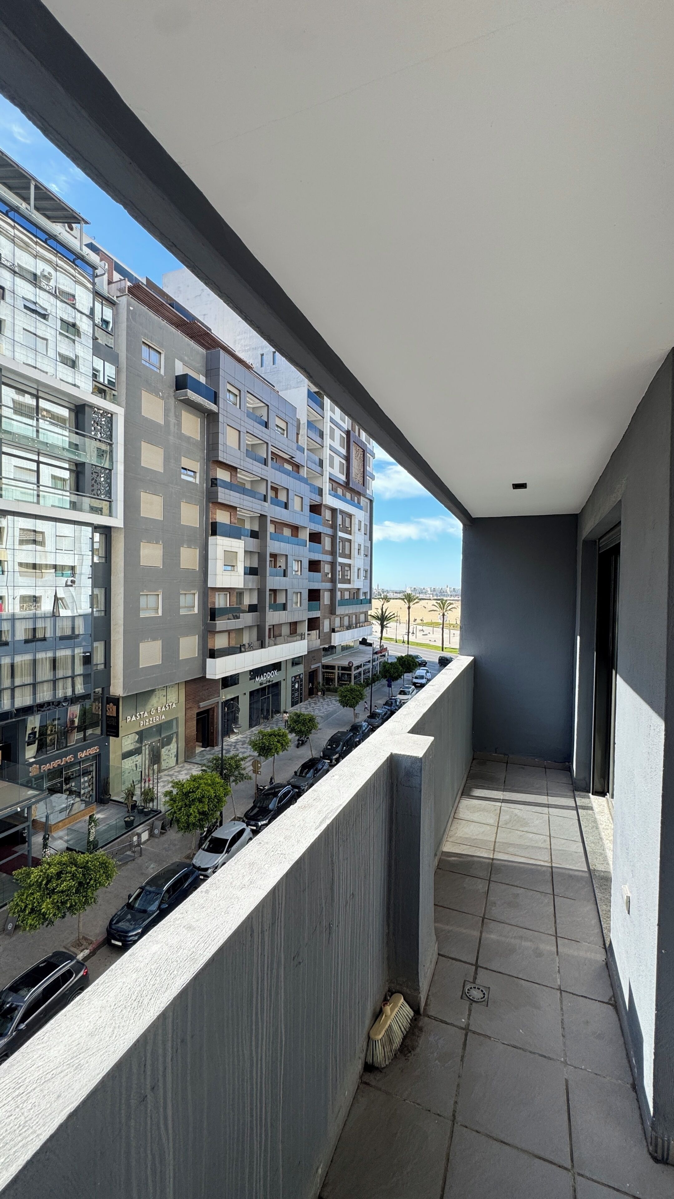 Un balcon donnant sur un paysage urbain, avec des bâtiments et des voitures garées.