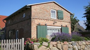 A brick house with a stone wall in front, a wooden fence, and flowering plants. - Holiday home with 1 bedroom (Ostseebad Wustrow)