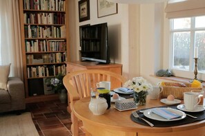 A cozy living room with a wooden bookshelf, a television, and a dining area with a table set for breakfast.
