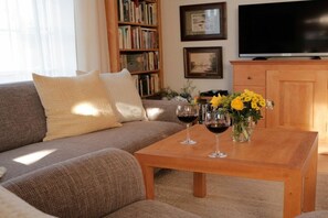 A living room with a sofa, a coffee table with wine glasses and flowers, a bookshelf, and a TV.