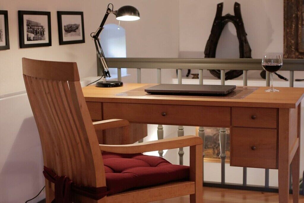 Un bureau en bois avec un ordinateur portable, une lampe et un verre à vin.