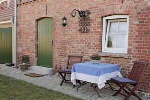 A brick building with a green door, a window, and a table with a blue and white tablecloth. - Holiday home with 1 bedroom (Ostseebad Wustrow)