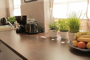 A kitchen with a coffee maker, a kettle, and potted plants on the counter.