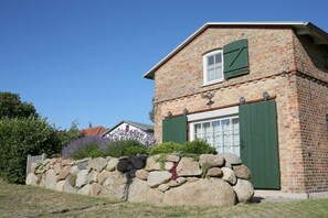 A brick house with a stone wall in front, a window with shutters, and a door with a green shutter. - Holiday home with 1 bedroom (Ostseebad Wustrow)